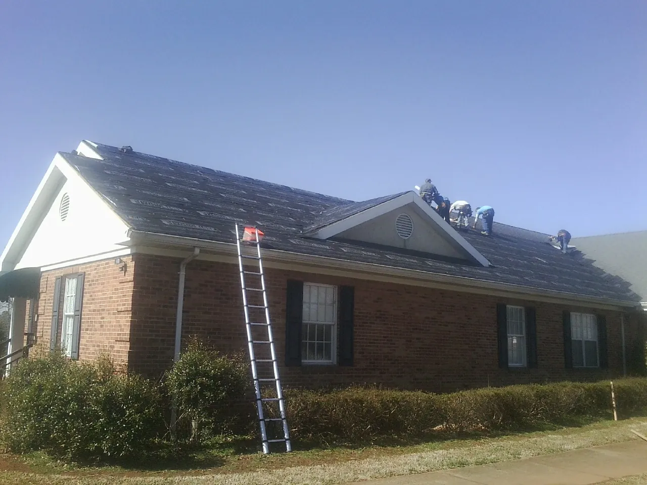 Crew tearing shingles off a brick ranch roof with a ladder set — Metal Roof Repair work by our crew in Orrtanna
