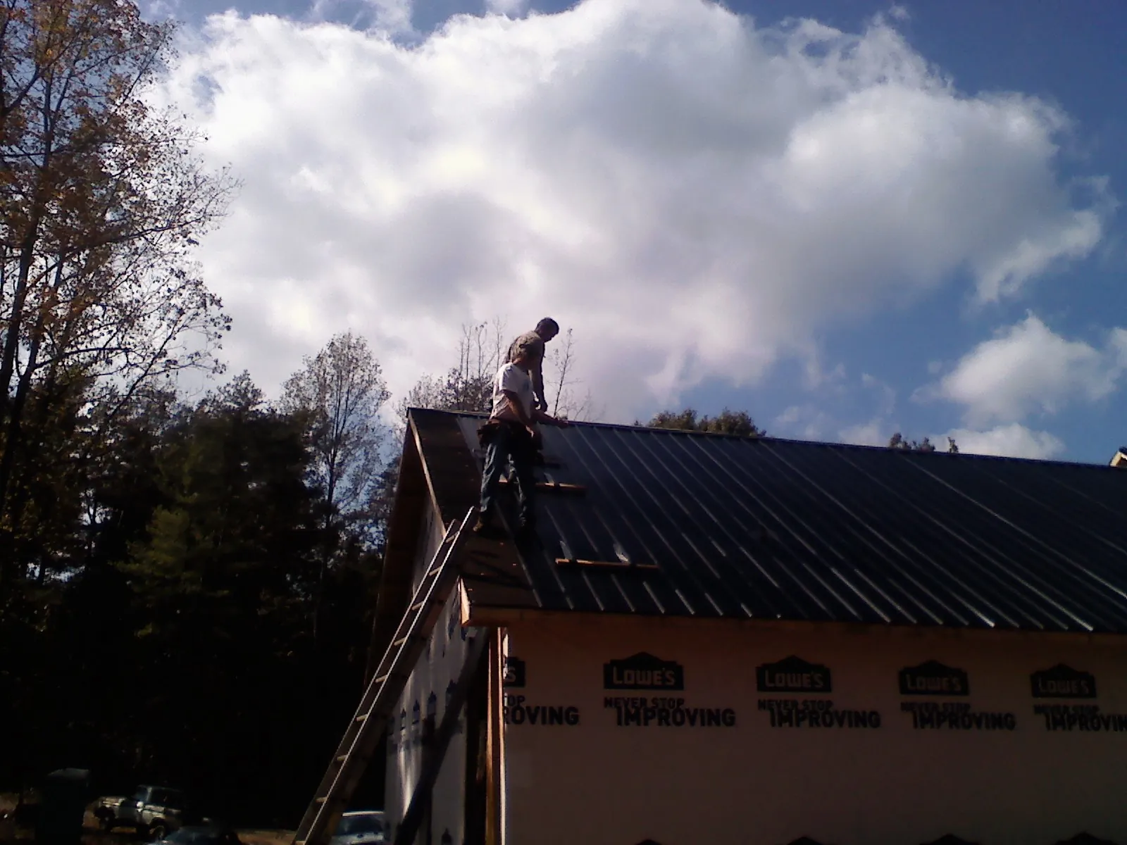 Roofer fastening dark metal panels high against a cloudy sky, from a Roof Inspection job in Orrtanna