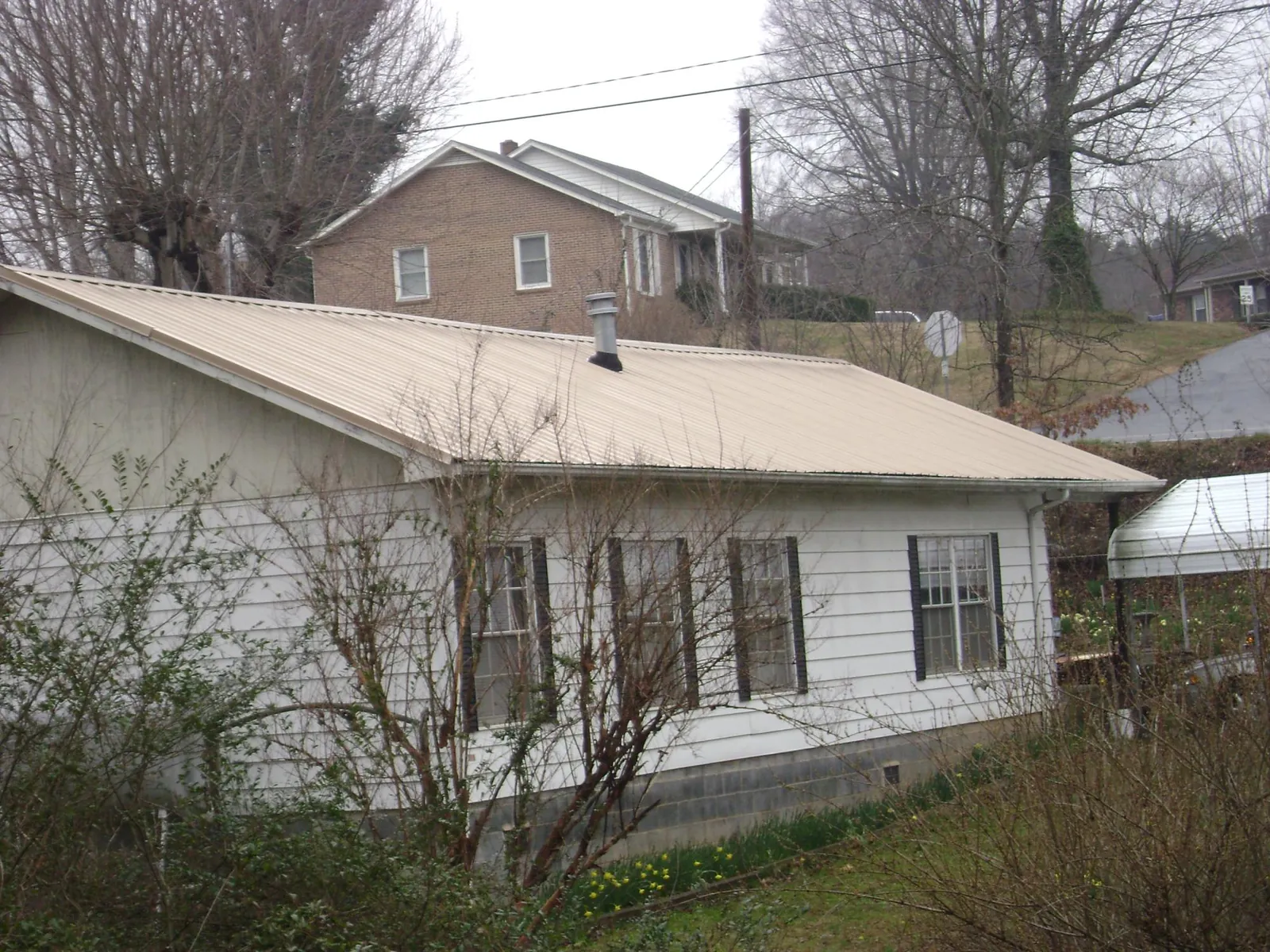 Tan metal roof on a white sided house set into a hillside — Commercial Roofing by Roofing Brothers in Orrtanna